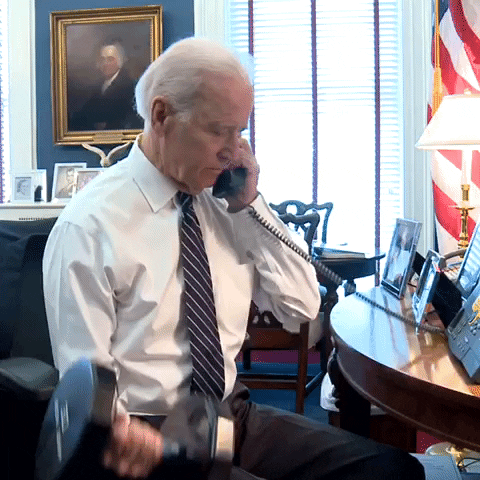 President Joe Biden sitting at his desk on a call doing bicep curls with a dumbbell 